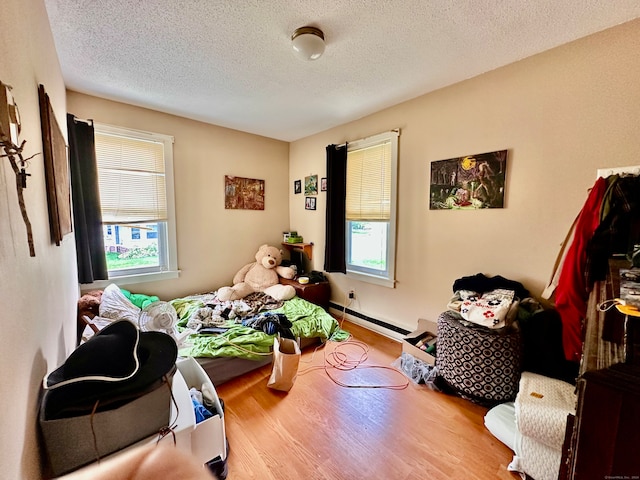 bedroom with light hardwood / wood-style floors, a textured ceiling, baseboard heating, and multiple windows