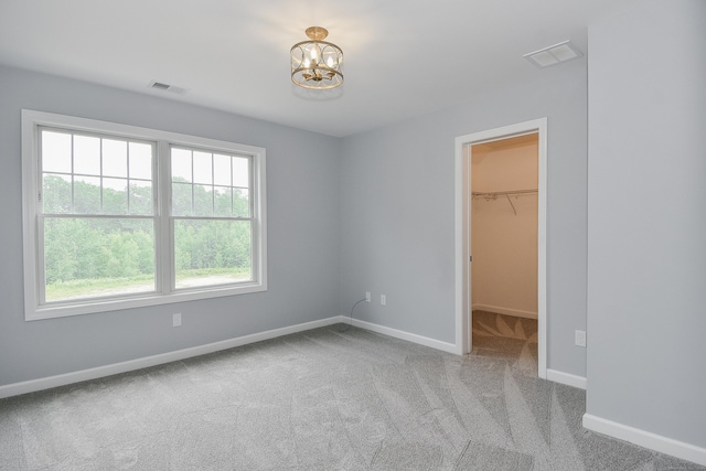 unfurnished bedroom featuring a walk in closet, light carpet, a closet, and a notable chandelier