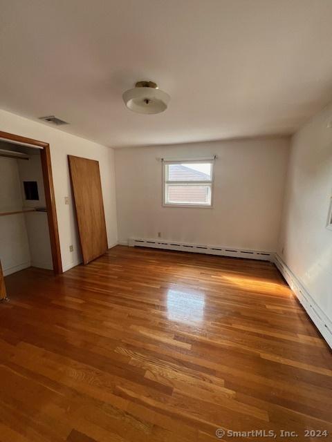 unfurnished bedroom with baseboard heating and wood-type flooring