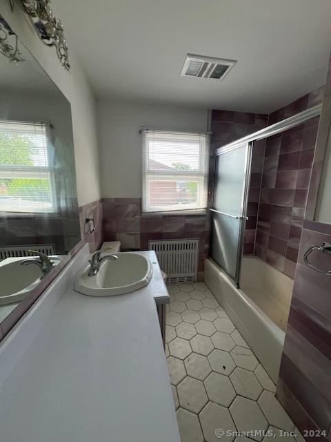 bathroom featuring a healthy amount of sunlight, radiator heating unit, combined bath / shower with glass door, and vanity