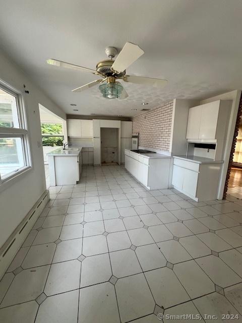 kitchen featuring ceiling fan, a baseboard radiator, sink, and white cabinets