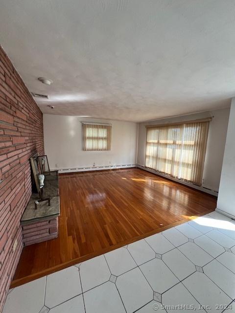 unfurnished living room with tile patterned floors, brick wall, a fireplace, and a wealth of natural light