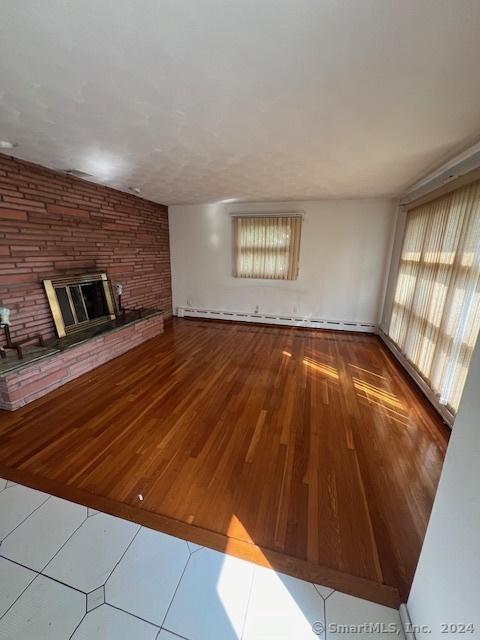 unfurnished living room with hardwood / wood-style floors, a fireplace, brick wall, and baseboard heating