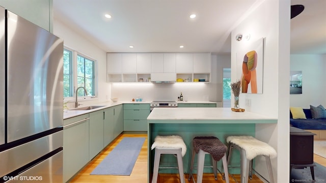 kitchen featuring stainless steel appliances, sink, light hardwood / wood-style flooring, green cabinets, and a kitchen breakfast bar