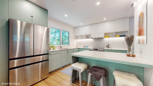 kitchen featuring appliances with stainless steel finishes, light wood-type flooring, green cabinetry, and a breakfast bar