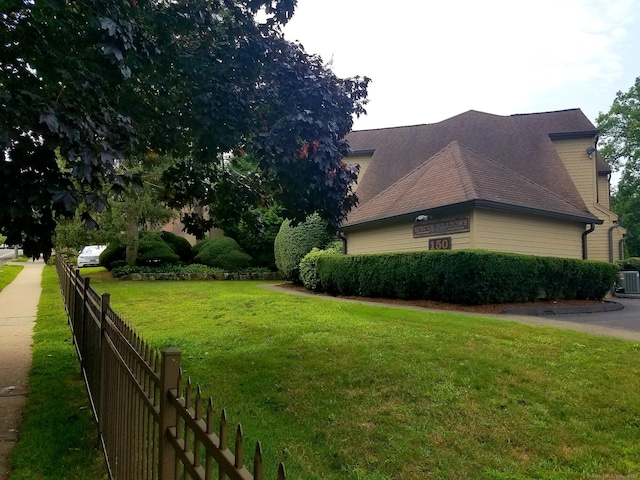 view of home's exterior with a yard, roof with shingles, fence, and central AC unit