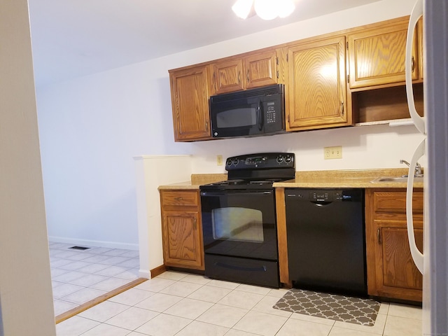 kitchen with light tile patterned floors, baseboards, light countertops, black appliances, and a sink