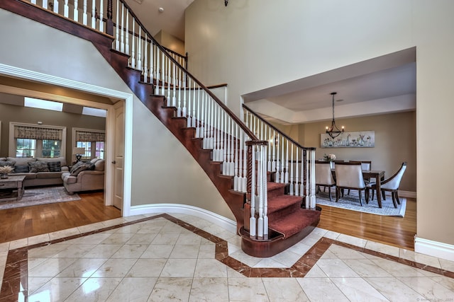 stairway with a towering ceiling, hardwood / wood-style flooring, and an inviting chandelier