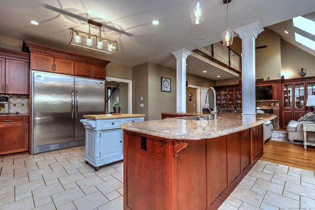 kitchen with sink, decorative columns, built in refrigerator, ceiling fan, and a kitchen island with sink