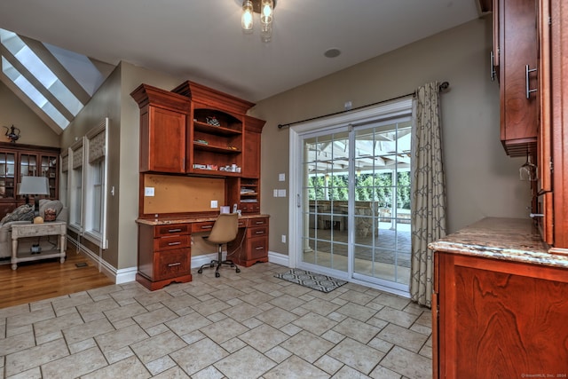 home office featuring vaulted ceiling, built in desk, and light hardwood / wood-style floors