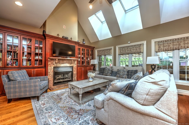 living room featuring light hardwood / wood-style floors, a high end fireplace, high vaulted ceiling, and a skylight