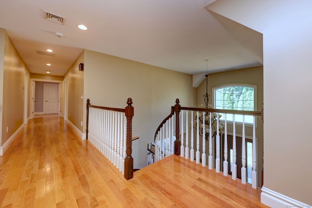 hall with light wood-type flooring and an inviting chandelier