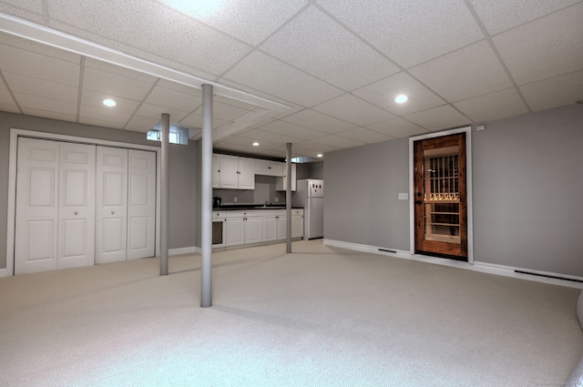 basement featuring white fridge, a drop ceiling, and light carpet