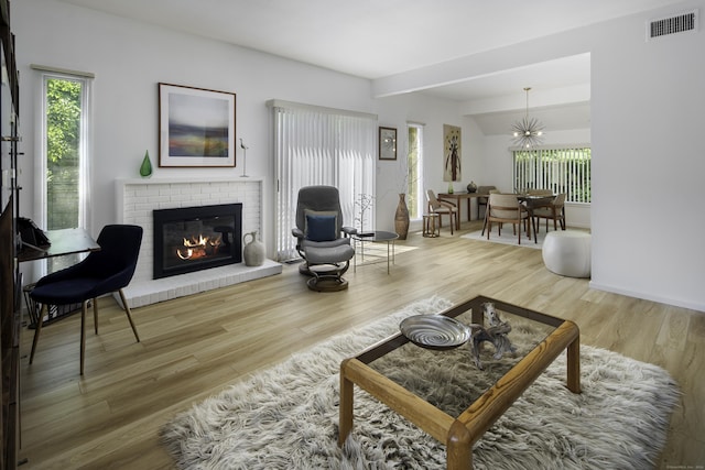 living room with beamed ceiling, hardwood / wood-style floors, a brick fireplace, and a notable chandelier