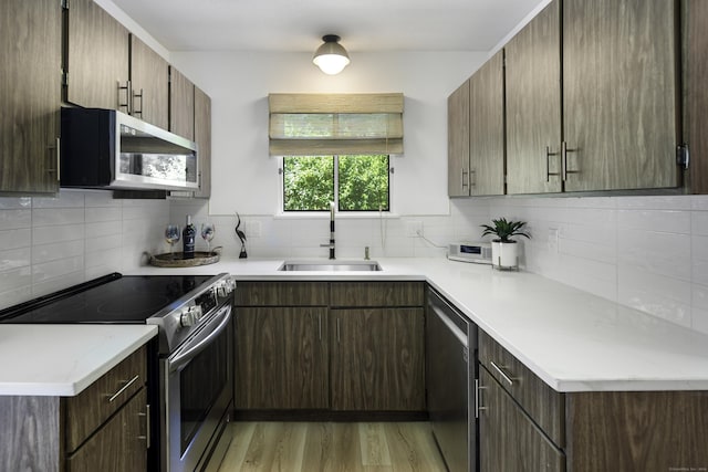 kitchen featuring sink, appliances with stainless steel finishes, light stone counters, light hardwood / wood-style floors, and decorative backsplash