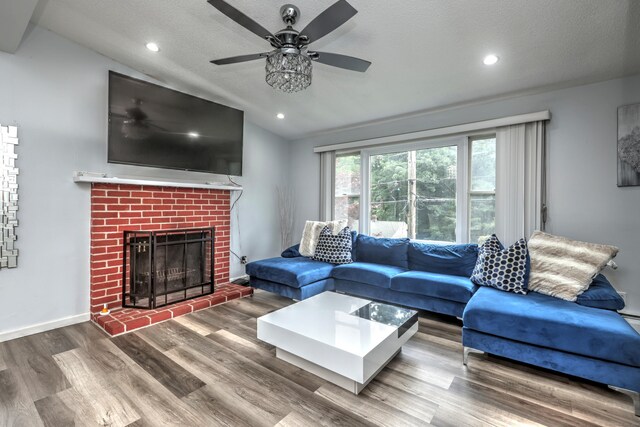 living room with vaulted ceiling, hardwood / wood-style floors, a textured ceiling, a brick fireplace, and ceiling fan