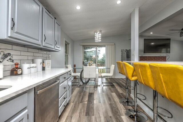 kitchen featuring lofted ceiling, dark wood-type flooring, backsplash, ceiling fan, and stainless steel dishwasher