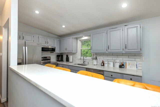 kitchen with stainless steel appliances, sink, lofted ceiling, backsplash, and gray cabinetry