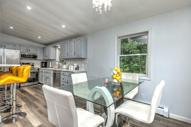 dining space with a textured ceiling, an inviting chandelier, dark wood-type flooring, vaulted ceiling, and sink