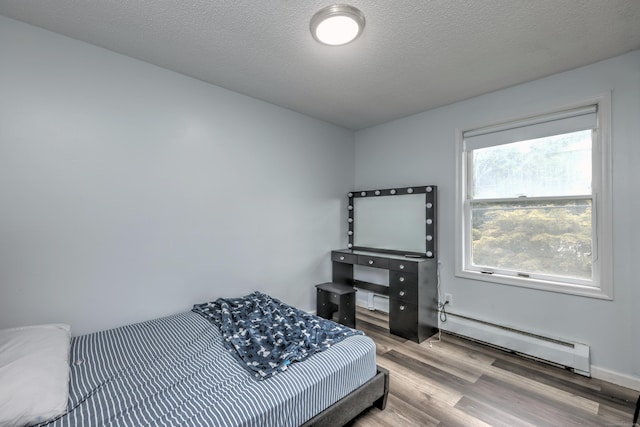 bedroom featuring a textured ceiling, a baseboard heating unit, and hardwood / wood-style floors