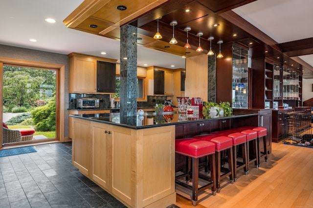 kitchen featuring plenty of natural light, light brown cabinetry, hardwood / wood-style flooring, and a breakfast bar area