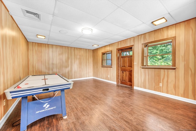 recreation room featuring a paneled ceiling, wooden walls, and hardwood / wood-style floors