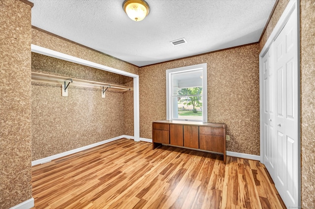 unfurnished bedroom with light hardwood / wood-style flooring, a closet, a textured ceiling, and crown molding