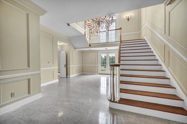 staircase with a notable chandelier, ornamental molding, french doors, a textured ceiling, and light tile patterned floors