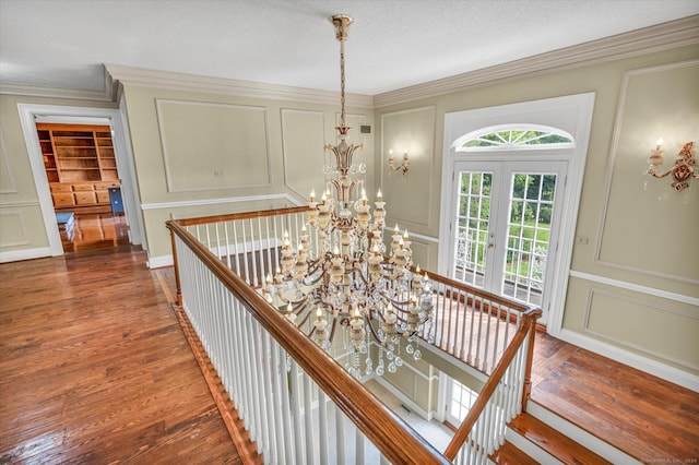 stairs with a notable chandelier, hardwood / wood-style floors, and ornamental molding