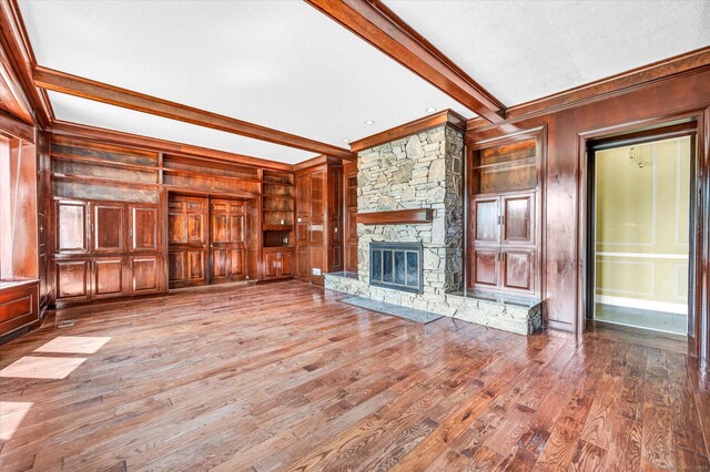 unfurnished living room featuring beam ceiling, a fireplace, hardwood / wood-style flooring, and wooden walls