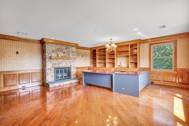 kitchen featuring hanging light fixtures, wooden walls, hardwood / wood-style floors, a center island, and a stone fireplace