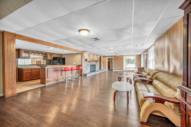 living room featuring a stone fireplace, a paneled ceiling, and hardwood / wood-style floors