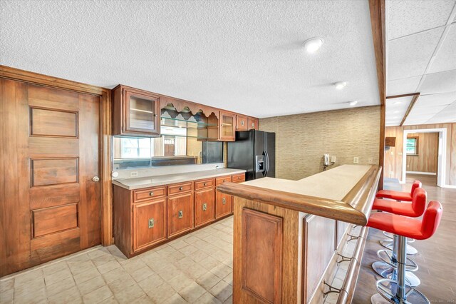 kitchen with a kitchen bar, a textured ceiling, black fridge with ice dispenser, and light tile patterned floors