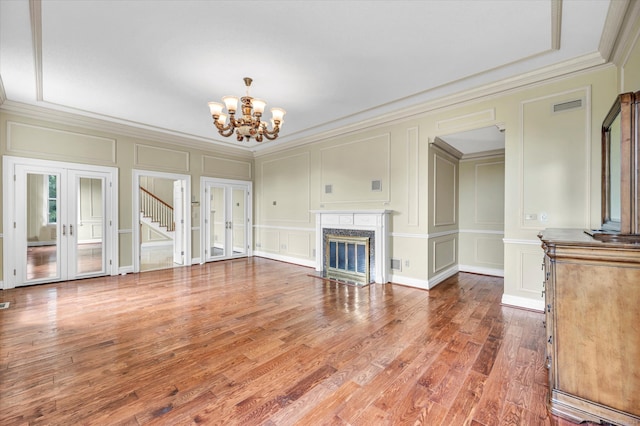 unfurnished living room with a notable chandelier, wood-type flooring, crown molding, french doors, and a premium fireplace