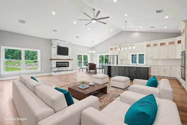 living room with ceiling fan with notable chandelier, a large fireplace, plenty of natural light, and light hardwood / wood-style floors