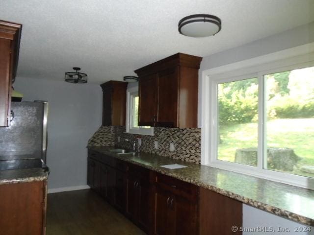 kitchen with backsplash, dark wood-type flooring, baseboards, freestanding refrigerator, and a sink