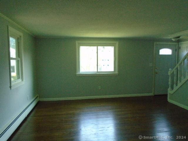 unfurnished room featuring a baseboard heating unit, baseboards, dark wood-style floors, and stairway