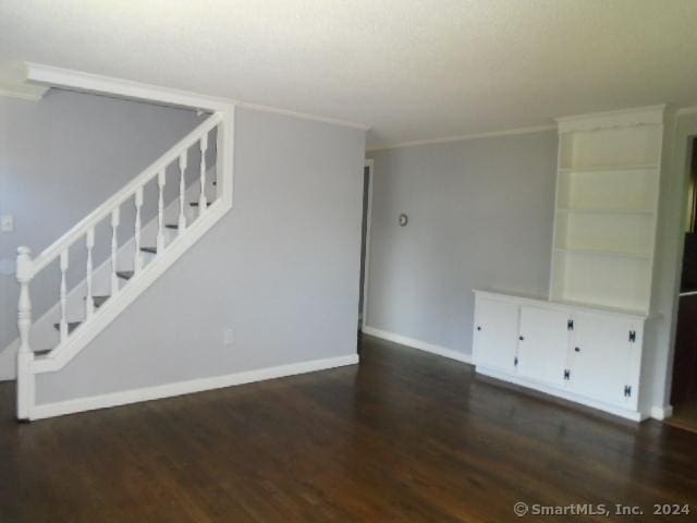 unfurnished living room featuring stairs, crown molding, wood finished floors, and baseboards