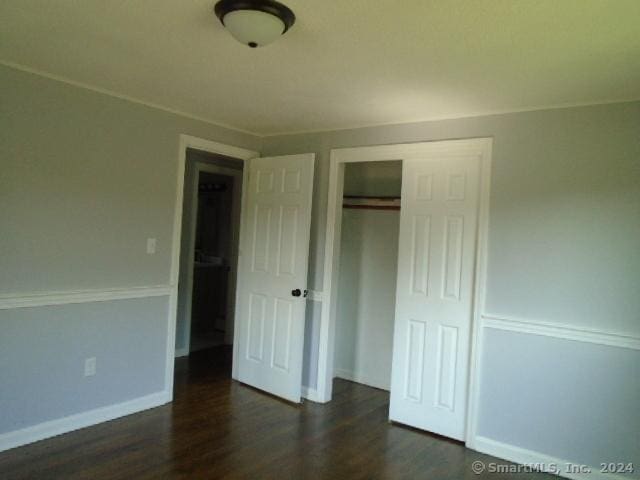 unfurnished bedroom with baseboards, dark wood-style flooring, and a closet