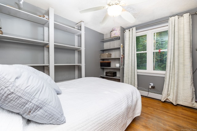 bedroom with a baseboard heating unit, ceiling fan, and hardwood / wood-style floors