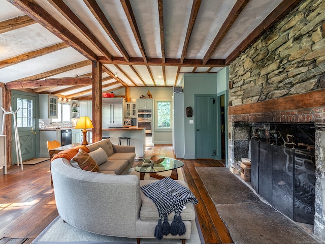 living room with vaulted ceiling with beams, a stone fireplace, and hardwood / wood-style flooring