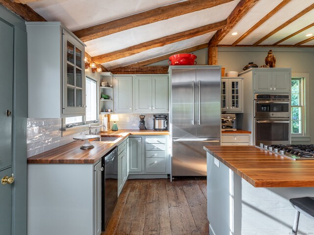 kitchen featuring tasteful backsplash, sink, vaulted ceiling with beams, appliances with stainless steel finishes, and butcher block countertops