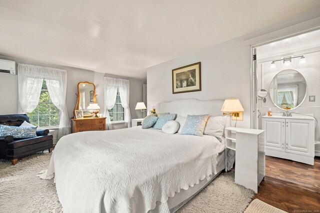 bedroom with connected bathroom, dark wood-type flooring, and a wall unit AC