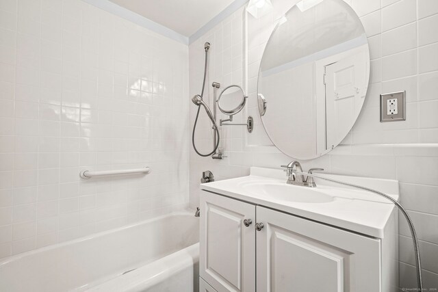 bathroom with tile walls, tiled shower / bath, and vanity