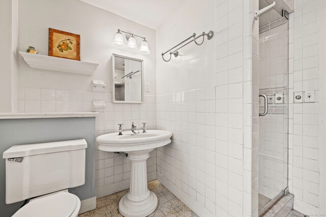 bathroom with tile walls, tile patterned flooring, toilet, and a shower with door