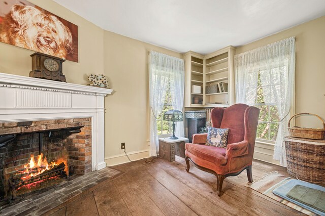 living area with wood-type flooring, a wealth of natural light, and a brick fireplace