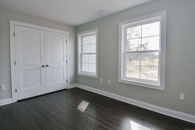 unfurnished bedroom with visible vents, baseboards, a closet, and dark wood finished floors