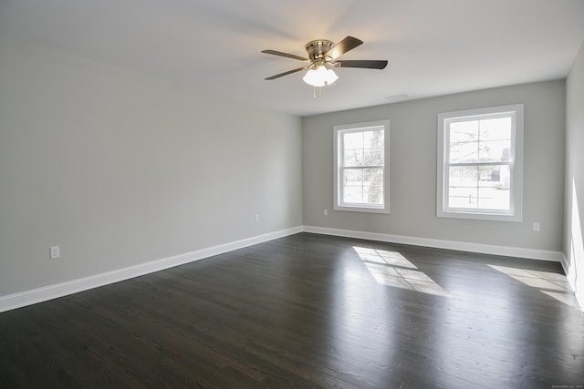 empty room with dark wood finished floors, a ceiling fan, and baseboards