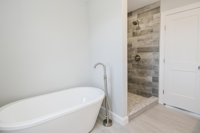 full bathroom featuring a freestanding bath, tiled shower, and baseboards