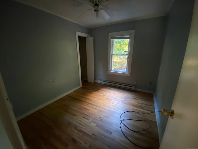 spare room featuring ceiling fan, a baseboard heating unit, and hardwood / wood-style floors